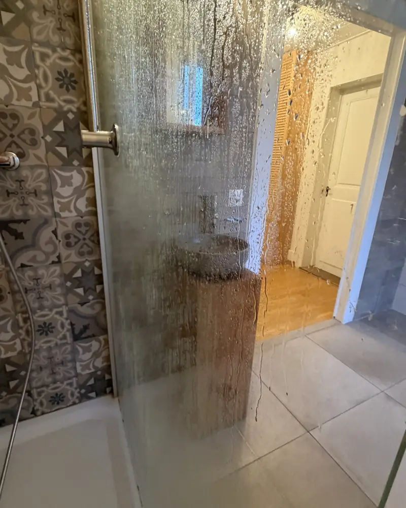 Paroi de douche en verre avant détartrage, traces de calcaire sur le verre, fin de bail à Romont